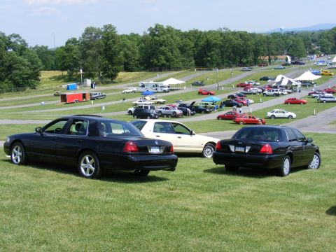 1997 Mercury Grand Marquis - Several Mercury Grand Marquis sedans are parked on a grassy field at an outdoor event with tents and other vehicles visible.
