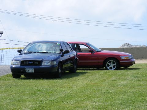 1997 Mercury Grand Marquis - Two sedans are parked on a grassy area with a cloudy sky overhead.