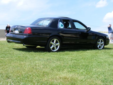 1997 Mercury Grand Marquis - Black 1997 Mercury Grand Marquis sedan viewed from the side, parked on a grassy field under a blue sky.