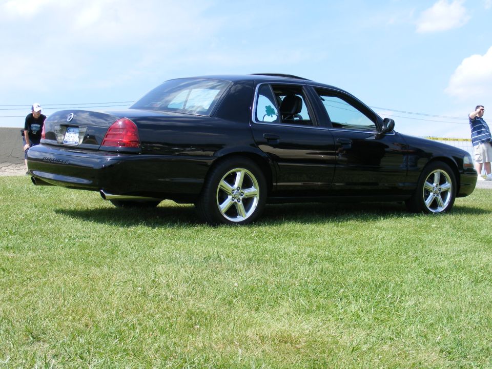 1997 Mercury Grand Marquis sedan, black, parked on grass with two people visible in background