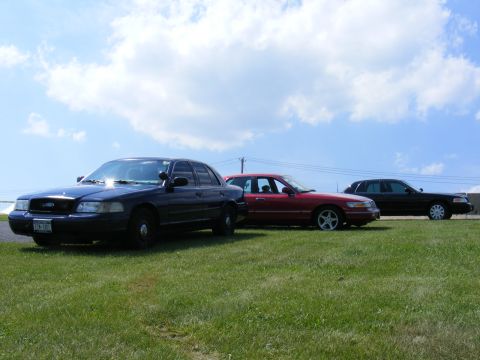 1997 Mercury Grand Marquis - Three sedans, including a 1997 Mercury Grand Marquis, are parked on a grassy field.