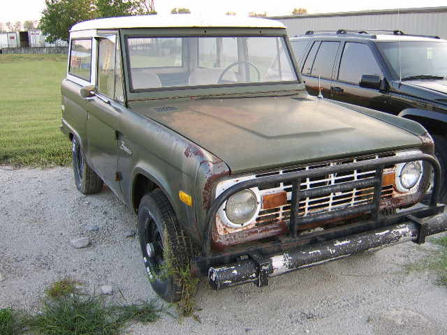 Green 1976 Ford Bronco with white roof, rusty front end, and black grille guard