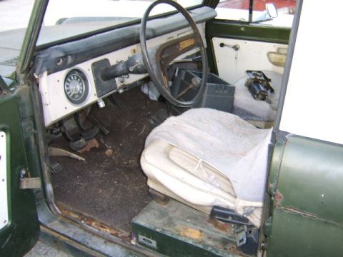 1976 Ford Bronco - The interior of a green vehicle shows a worn seat, dashboard, and steering wheel.