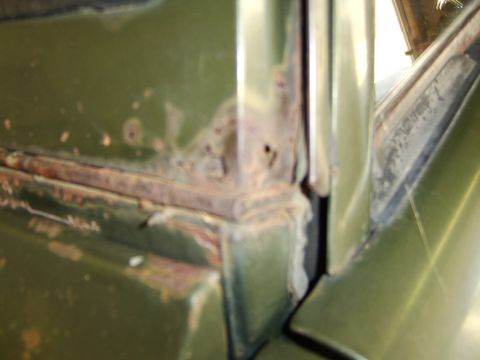 1976 Ford Bronco - Close-up view of rust damage on a green vehicle's body corner, indicating wear and tear.