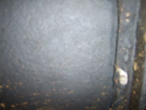 1976 Ford Bronco - A close-up view of a textured metal surface, possibly part of a vehicle's undercarriage, showing rust and a bolt head.