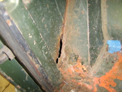 1976 Ford Bronco - Close-up of a heavily rusted green metal panel, showing a large hole and orange undercoating. The registry claims this is a 1976 Ford Bronc…