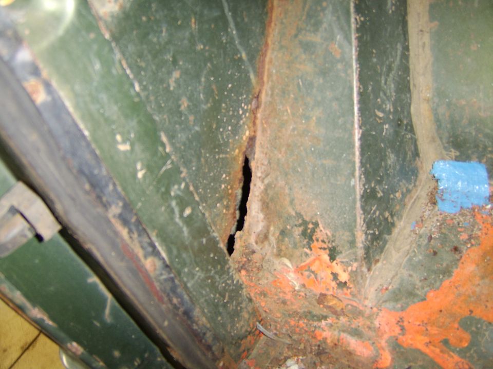 Rusted green metal panel with hole and orange undercoating