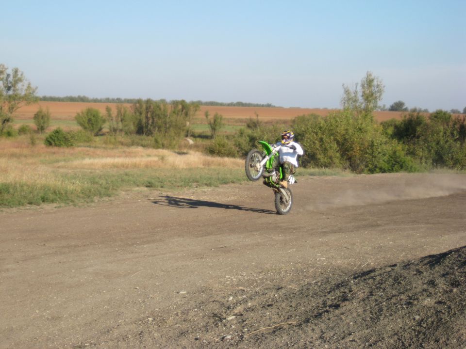 Green dirt bike performing a wheelie on a dirt track