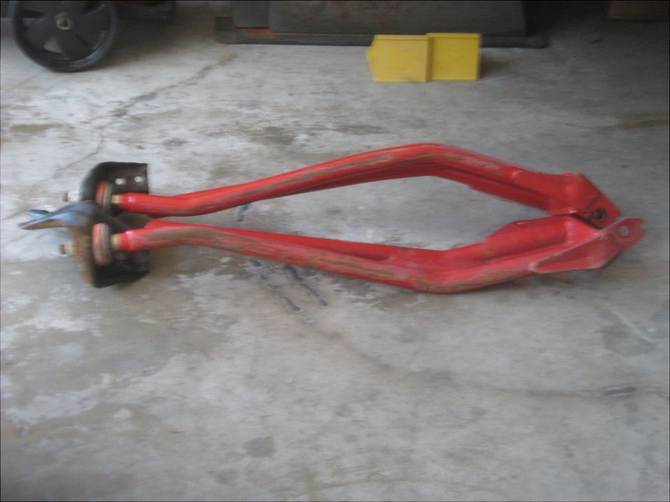 Red suspension control arms with metal brackets and bolts on a concrete floor