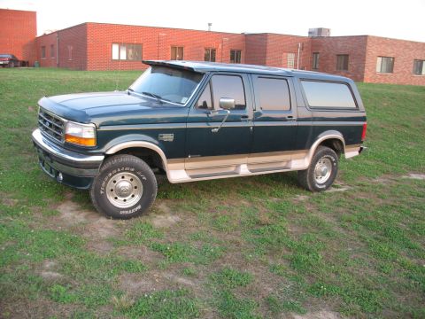 1995 Ford C-350 (Centurion Conversions) - Side view of a dark green and tan SUV with running boards parked on a grassy hill.