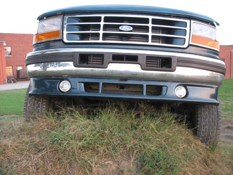 1995 Ford C-350 (Centurion Conversions) - The front grille and headlights of a Ford truck are visible, with the vehicle positioned on a grassy incline.