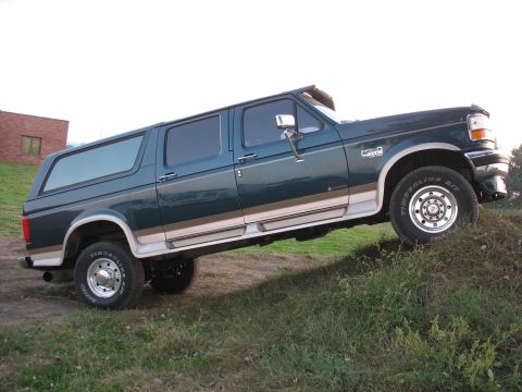 1995 Ford C-350 (Centurion Conversions) - This extended cab pickup truck with a camper shell is shown from the side on a grassy hill.