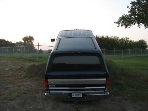 1995 Ford C-350 (Centurion Conversions) - The rear of a Ford Bronco with a camper shell is parked outdoors near a fence.