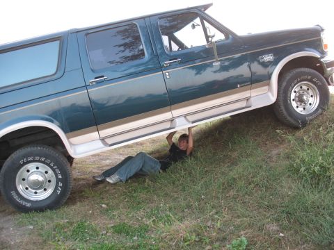 1995 Ford C-350 (Centurion Conversions) - A person lies under a teal and tan Ford F-Series truck with a camper shell, viewed from the side.