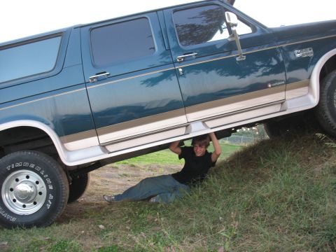 1995 Ford C-350 (Centurion Conversions) - A person is underneath a teal 1995 Ford C-350 Centurion Conversions SUV, which is parked on a grassy incline.