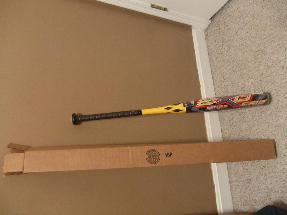 Baseball bat with yellow and black accents lies next to a long cardboard box on a carpeted floor