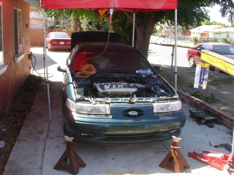 1993 Ford Taurus - Green 1993 Ford Taurus undergoing repairs under a red canopy, with a second vehicle visible in the background.