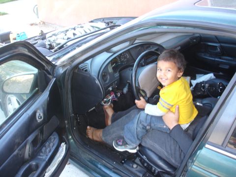 1993 Ford Taurus - A child sits on a lap in the driver's seat of a 1993 Ford Taurus, with the hood open and engine visible.