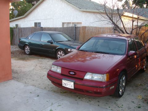 1993 Ford Taurus - A red 1993 Ford Taurus is parked in front of a green sedan in a residential driveway.
