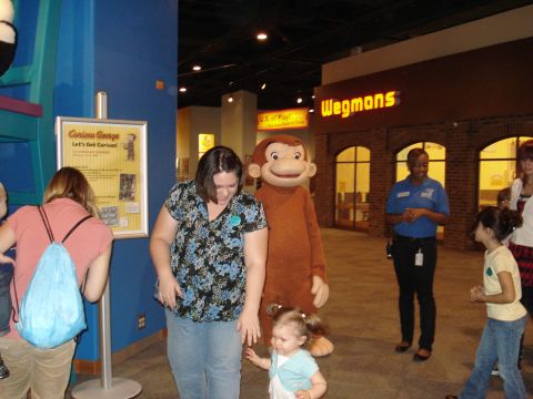 2000 Ford Crown Victoria - A museum exhibit features a Curious George mascot interacting with visitors, including a woman and a young child.