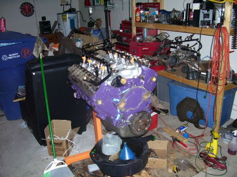 1991 Ford Bronco - A purple-painted V8 short block sits on an orange engine stand in a home garage, viewed from the front with the timing cover and harmonic b…
