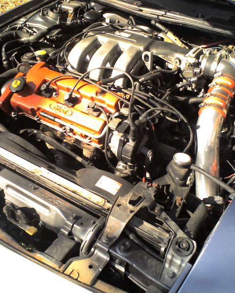 1994 Ford Probe - The engine bay of a 1994 Ford Probe is visible, a V6 engine with orange valve covers and an aftermarket intake system.