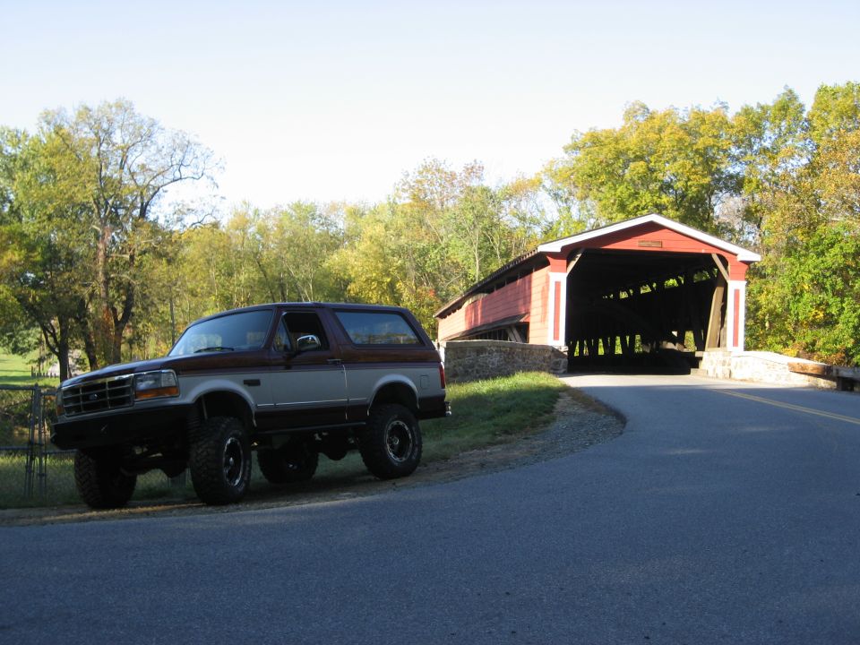 Brown and tan Ford Bronco parked on the side of a road next to a covered bridge