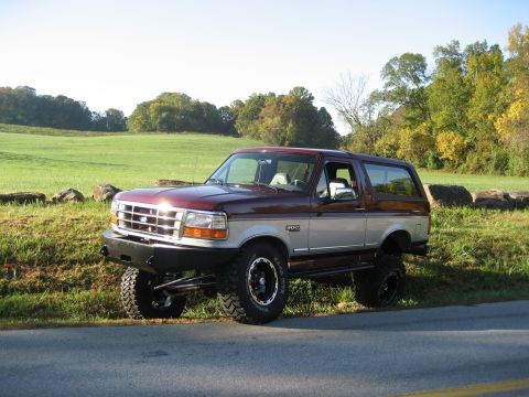 1996 Ford Bronco - Maroon and silver 1996 Ford Bronco parked roadside with a grassy field and trees in the background.