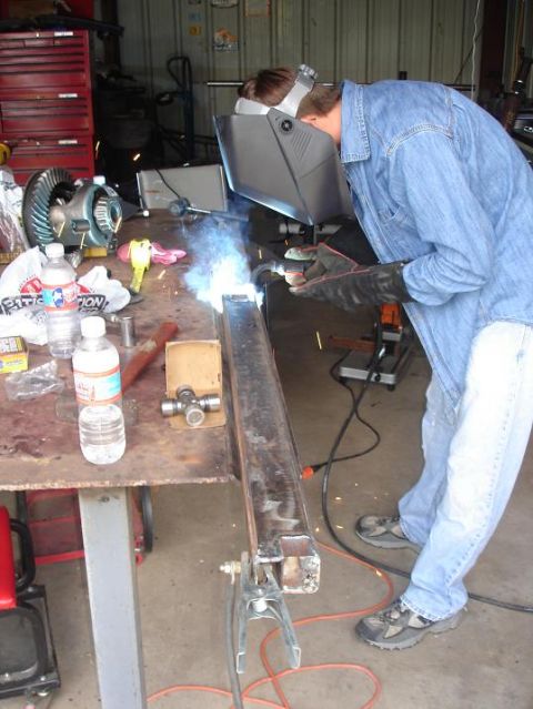 1996 Ford F-150 - A person welds a metal beam on a workbench, with automotive parts visible in the background.