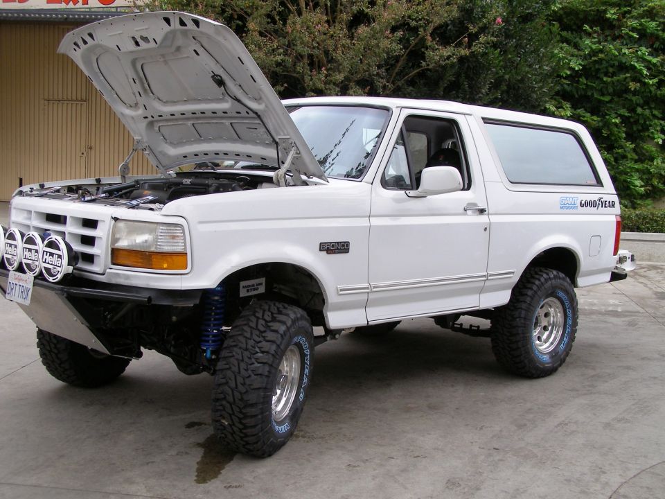 White Ford Bronco with hood up, off-road light bar, and lift kit parked outdoors