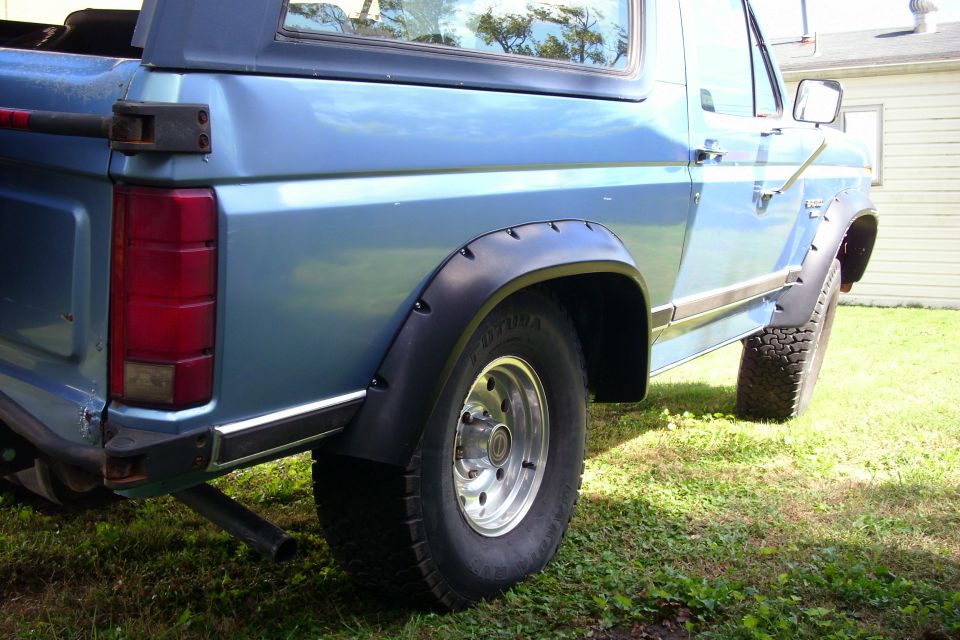 Rear quarter of a light blue SUV with black fender flares and chrome wheels on grass