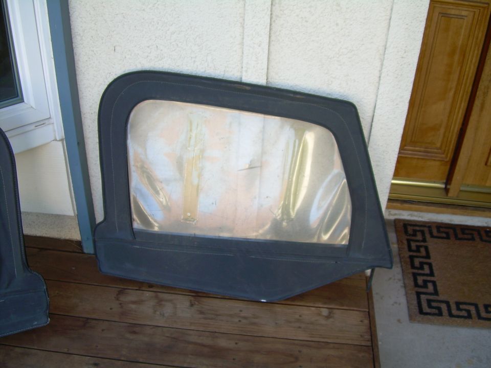 Black soft top window frame with clear plastic window, lying on wooden planks