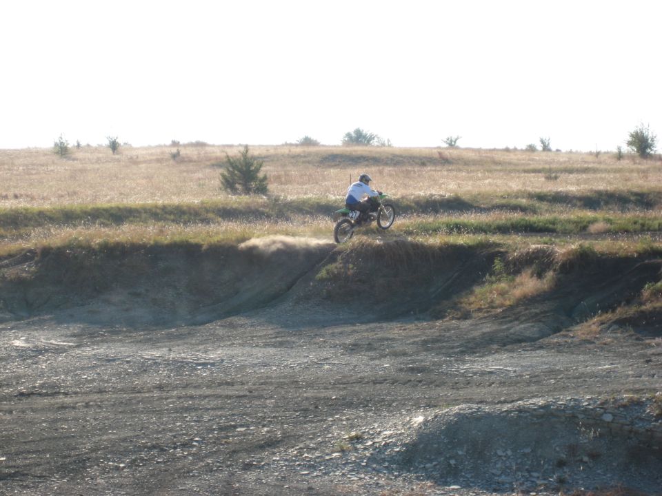Dirt bike rider kicking up dust on a dry, grassy hill