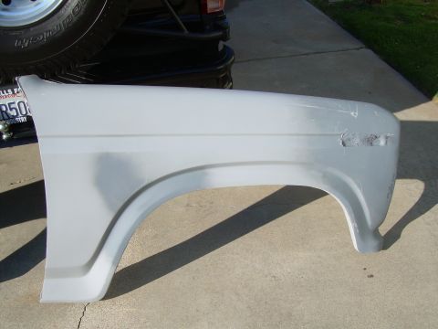 1986 Ford Bronco - A vehicle fender, prepped for paint, sits on a concrete surface with a spare tire visible in the background.