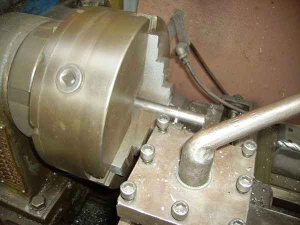 Metal lathe chuck holding a rod, with tool post and handle visible