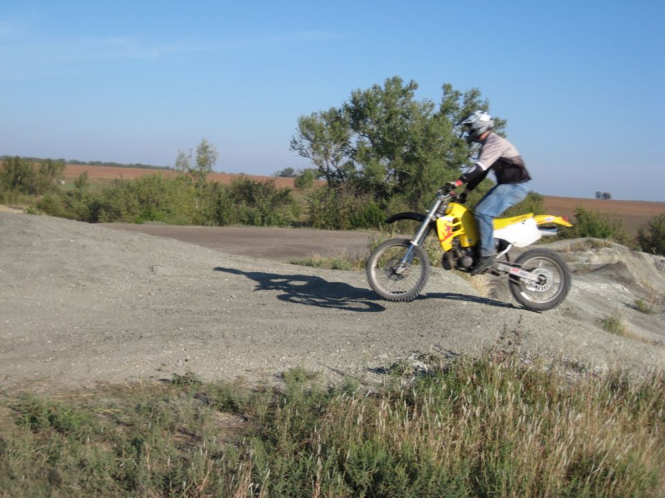 Guy on yellow dirt bike riding on a dirt track with trees and fields in background