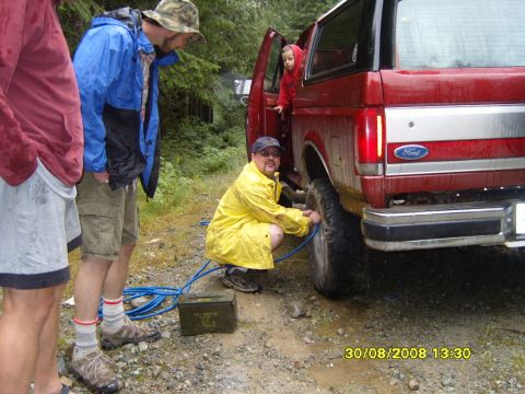 1989 Ford Bronco - A group of people are airing up the tire of a red 1989 Ford Bronco in a wooded area.
