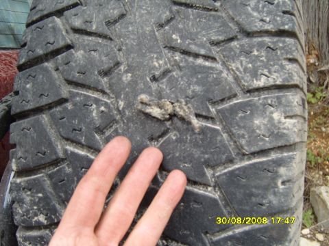 1989 Ford Bronco - Debris stuck in the tread of a tire, with a hand for scale. No vehicle is visible.
