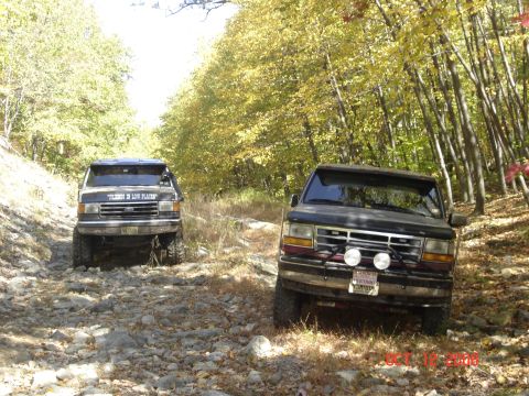 1994 Ford Bronco - Two Ford Broncos navigate a challenging, rocky path through a forest during the fall season.