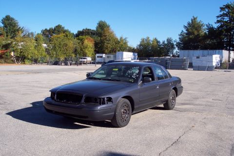 2001 Ford Crown Victoria - Dark gray 2001 Ford Crown Victoria with missing front end parts sits in a lot.