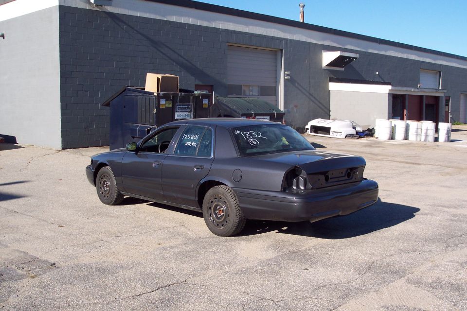 Dark gray 2001 Ford Crown Victoria, rear bumper missing, parked outside a building