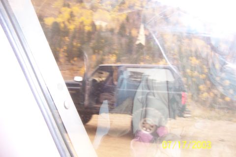 1996 Ford Bronco - A dark SUV is parked on a dirt road, with autumn foliage visible on the hills behind it.