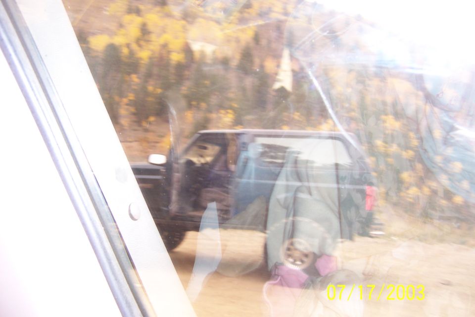 dark SUV parked on dirt road with trees and hills in background