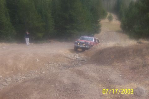 1996 Ford Bronco - A red SUV navigates a rough dirt path surrounded by trees.