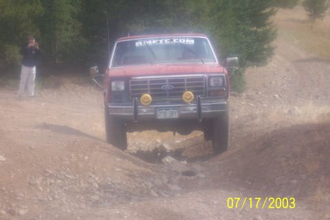 1996 Ford Bronco - A red Ford Bronco navigates a rocky off-road trail, its front grille two yellow smiley face lights.
