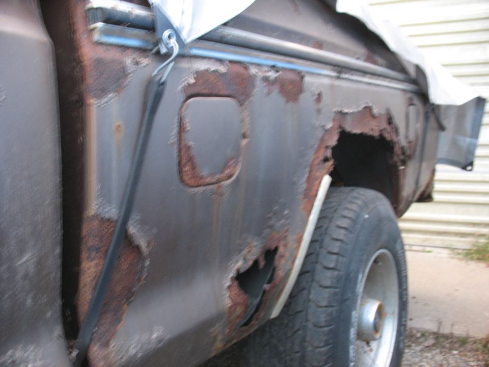Side view of a heavily rusted pickup truck bed with a gas cap door visible
