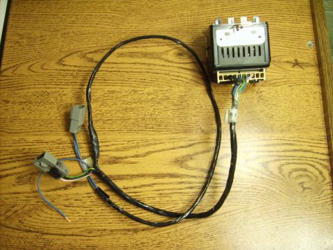 1982 Ford LTD Crown Victoria - Automotive electronic control module laid out on an oak table with its wiring pigtail, showing a black vented plastic housing with a white…