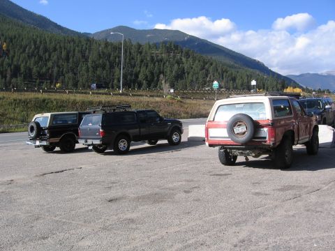1996 Ford Bronco - A red Ford Bronco is parked on asphalt with other vehicles, facing away from the camera, with mountains in the distance.