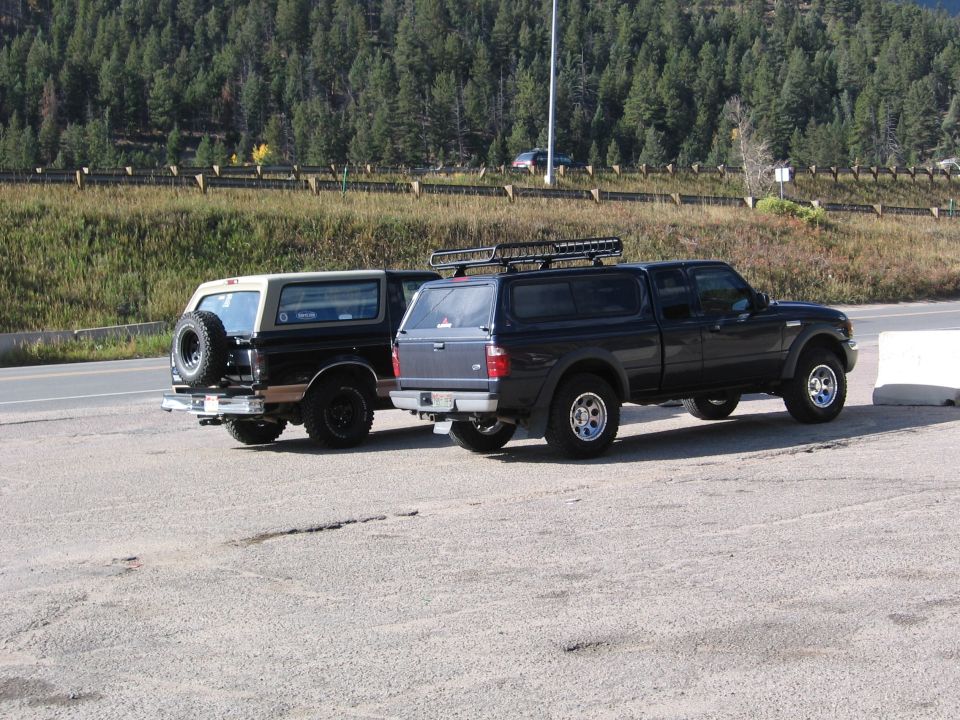 Two SUVs parked in a gravel lot with a wooded hillside behind them.