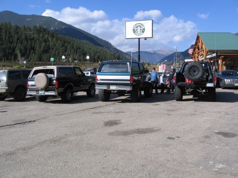 1996 Ford Bronco - A line of SUVs and trucks are parked in a lot in front of a Starbucks and a mountain range. The vehicles appear to be Ford Broncos and a pi…